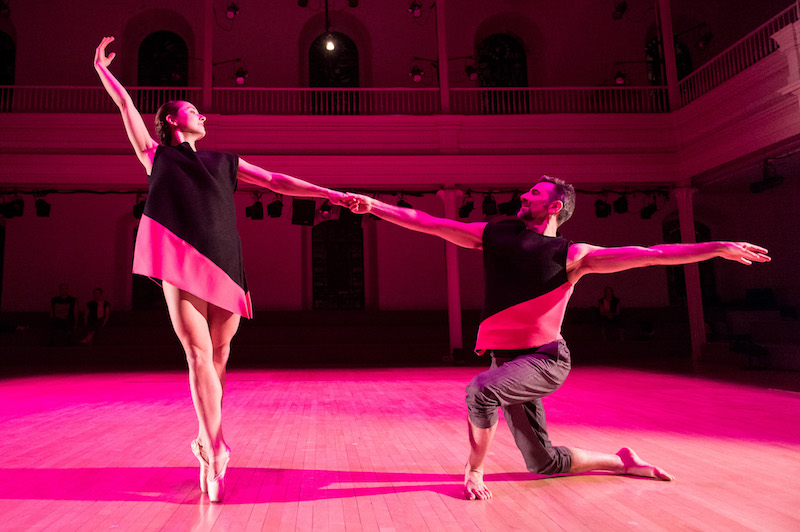 A woman in a black tunic is en pointe holds the hand of her partner who is on one knee